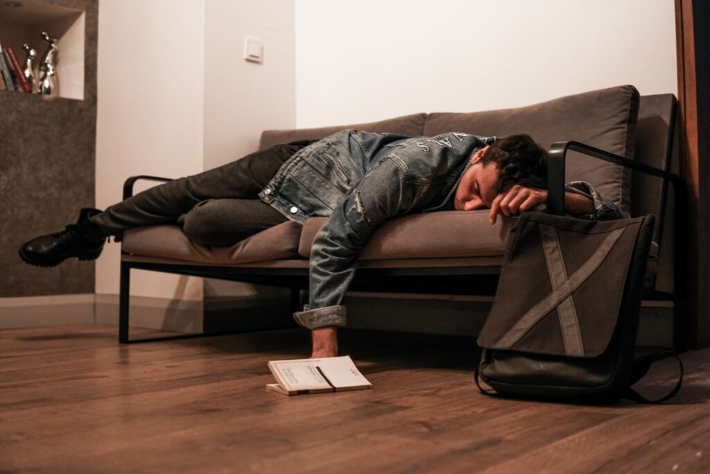 man in black jacket and blue denim jeans lying on brown leather couch