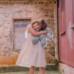 girl in white dress standing beside red wooden door during daytime